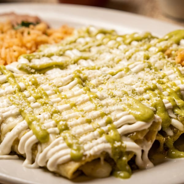 Enchiladas with green sauce, sour cream, and cheese, served with rice and refried beans.
