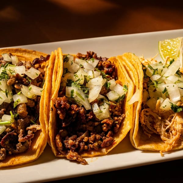 Three tacos, two with ground meat and one with shredded chicken, topped with onions, cilantro, and lime wedges.