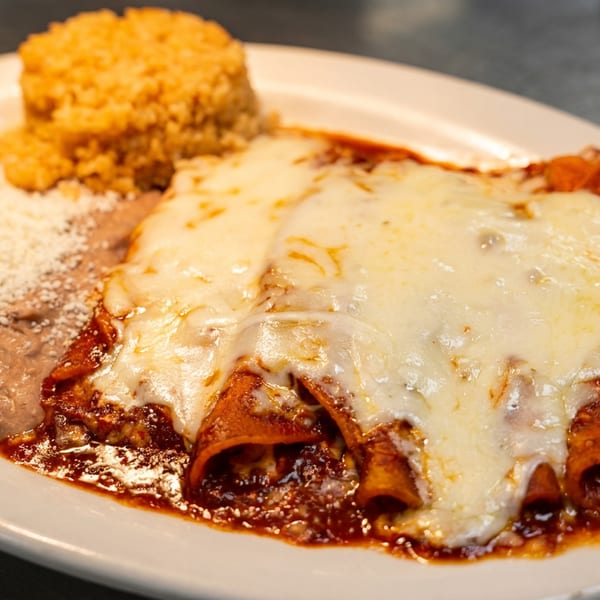 A plate of cheesy enchiladas with red sauce, refried beans, and a side of rice.